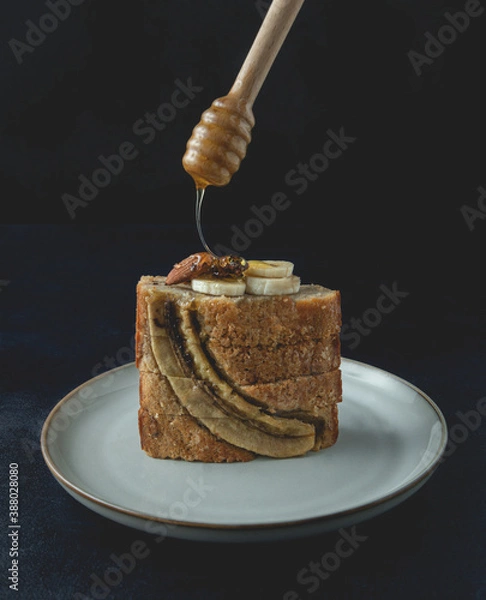 Obraz Slices of banana nut bread loaf with honey on top placed on the plate. An appetizing, soft bread texture, with crushed nut and honey aroma. Front view, close up.