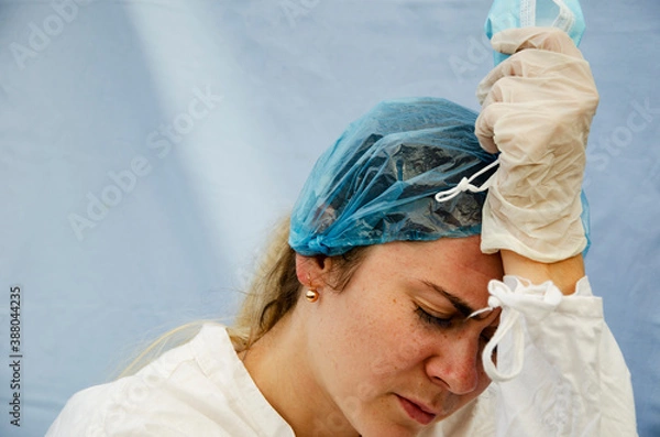Fototapeta A tired doctor after a hard day with coronavirus patients. An exhausted doctor from a large number of people infected with coronavirus. Doctor in a medical mask and gloves in a protective suit works 