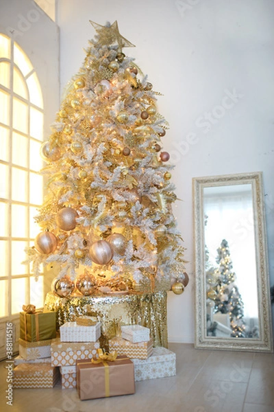 Obraz A Christmas tree with a Golden decoration is reflected in the mirror. New year, home decoration. Large window with yellow warm light, comfort in the living room, gift boxes