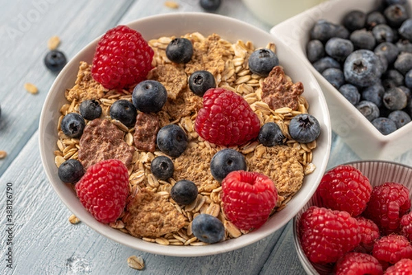 Fototapeta Granola with blueberries and raspberries in white bowl on dark white desk.