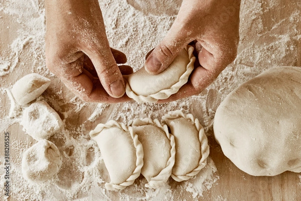 Fototapeta the cook holds dumplings, baker's hands, dough, hands in flour, dumplings, handmade dumplings, ravioli