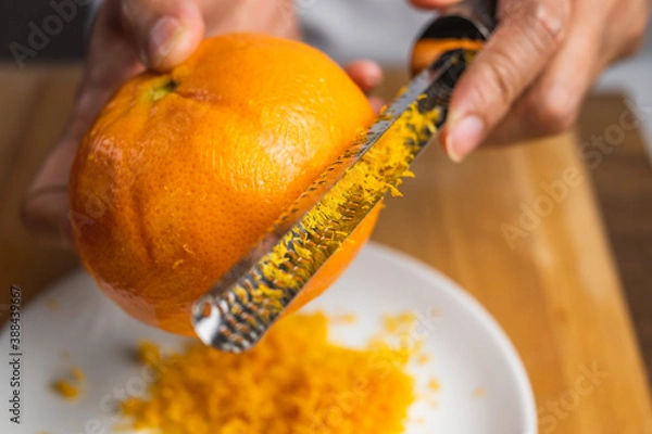 Obraz A zester zesting orange skin on a white plate on a wooden tabletop. 