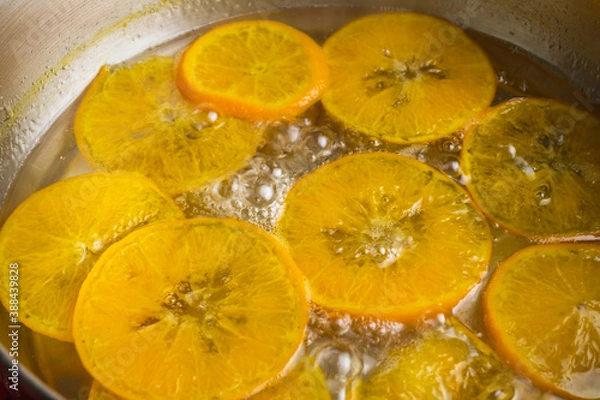 Fototapeta Orange slices cooking in bubbling hot syrup in a pot. Making candied orange slice for dessert decoration garnish.
