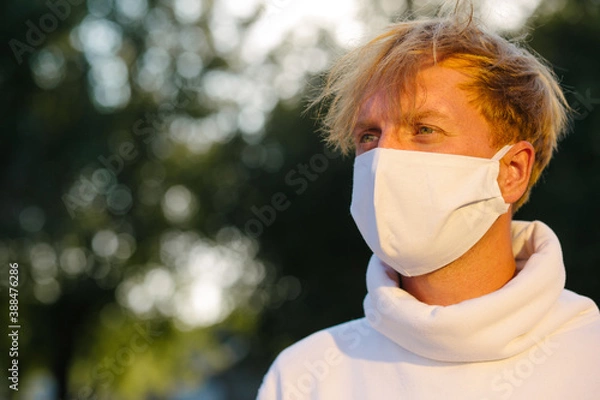 Obraz Portrait of a young man in a medical protective mask looking straight.