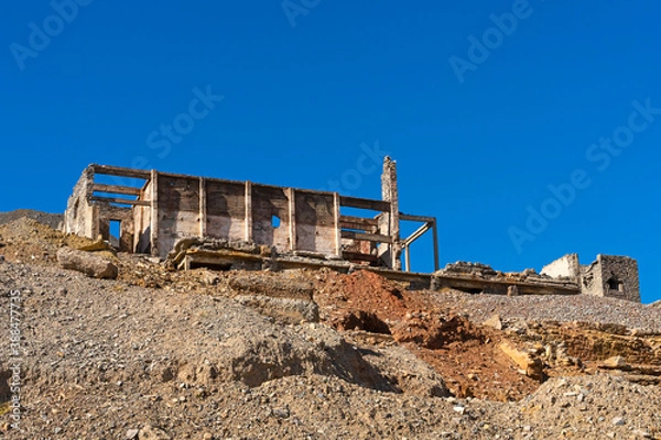 Fototapeta An old abandoned factory in the mountains. Fragments of destroyed buildings. Mountains.Ruins of a poly metal factory.Abandoned industrial production.The ruins of a mining and processing plant.Blue sky