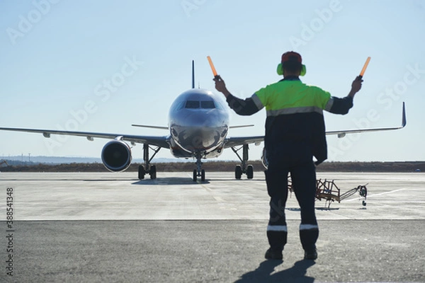 Fototapeta The runway traffic controller uses gestures and sticks to help the aircraft choose the correct trajectory around the airfield