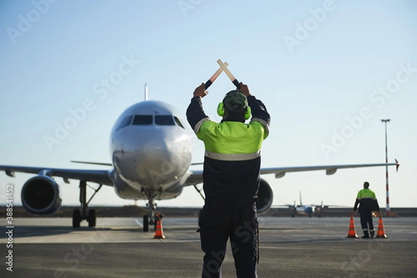 Fototapeta The runway traffic controller uses gestures and sticks to help the aircraft choose the correct trajectory around the airfield