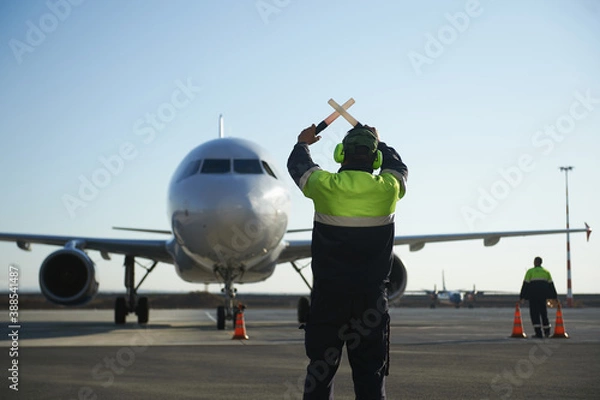Fototapeta The runway traffic controller uses gestures and sticks to help the aircraft choose the correct trajectory around the airfield
