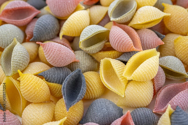 Fototapeta Colored Italian pasta in the shaped of seashells with yellow, pink, and purple colors. Textured background. Macro close up, selective focus.