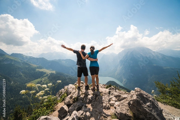 Fototapeta Girl and boy standing on the top of a cliff holding each other and spreading arms, beautiful scenery in the background