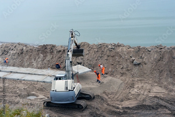 Fototapeta Russia, the city Zelenogradsk - 25.10.2020. Fortifying the beach, a Terex excavator works on the beach. Workers dismantle the old fortifications that held the slope. Equipment and workers fill a new c