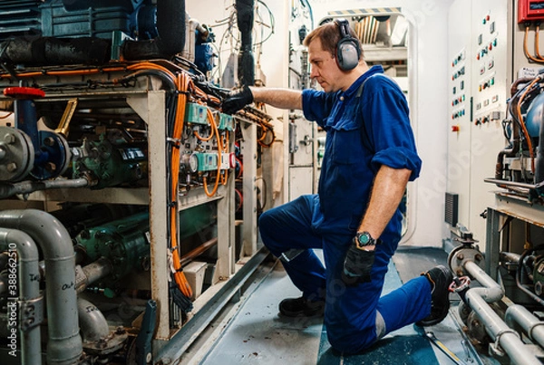 Fototapeta Marine engineer officer controlling vessel engines and propulsion in engine control room ECR. Ship onboard maintenance