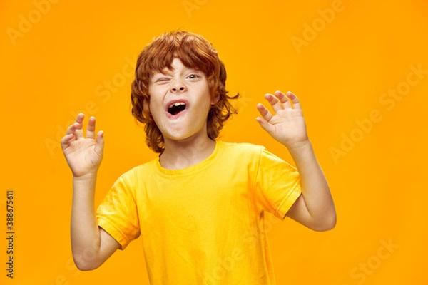 Fototapeta Nimble red-haired boy showing hands forward and yellow t-shirt Copy space
