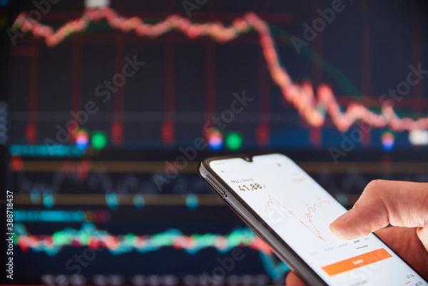 Fototapeta Investor analyzing stock market investments on a smartphone. Person trading stocks on a smartphone in front of a big screen with falling share prices. Stock market crash. US stock exchange.