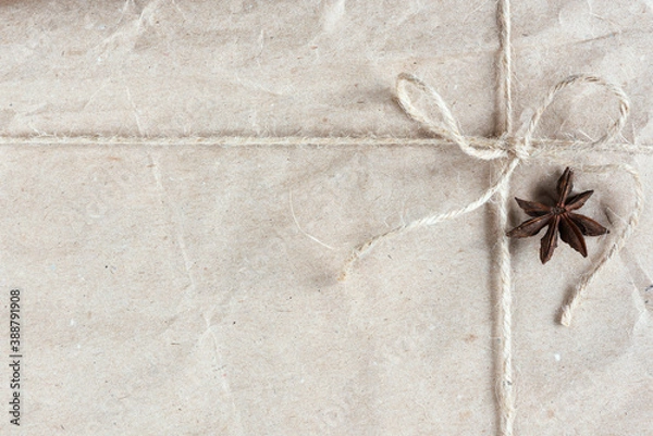 Obraz Eco-friendly Christmas gift wrapped in kraft paper with a star anise tied with twine close-up. Top view, copy space.