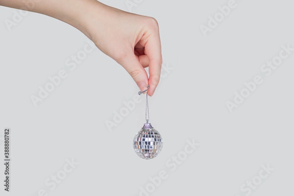 Fototapeta A white hand holds a silver mirror ball on a string