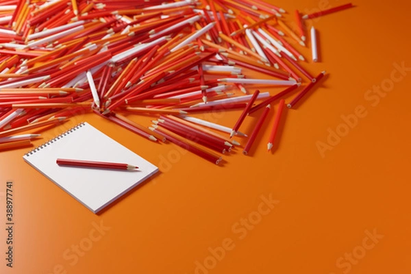 Fototapeta Pencils and sketchbook. Lots of pencils in warm colors next to a blank sketchbook on an orange background. 3D illustration