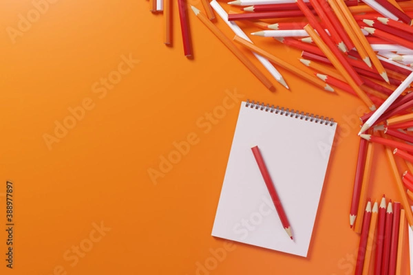 Fototapeta Pencils and sketchbook. Lots of pencils in warm colors next to a blank sketchbook on an orange background. 3D illustration