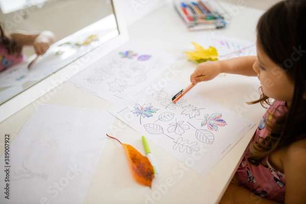 Fototapeta Little girl pointing at a paper sheet with coloring leaves images with a pen