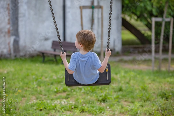 Fototapeta Little boy ride on a swing in the child playground. Little baby boy hand holding tightly on a metallic chain while going on a swing at a playground. Rear view