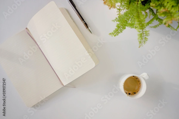 Fototapeta Top view of coffee cup and notebook on a white desk