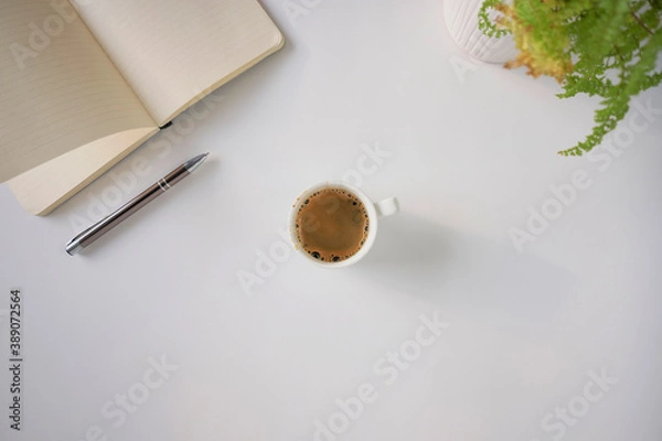 Fototapeta Top view of coffee cup and notebook on a white desk