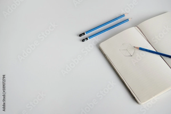 Fototapeta Notebook with a sketch and pencils on a white desk
