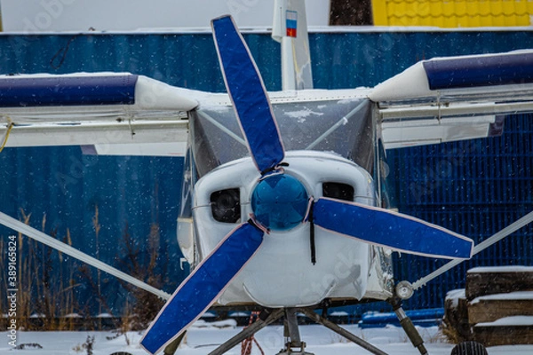 Fototapeta small aircraft with a propeller painted in bright colors in a case at the airfield or airport in the snow in winter
