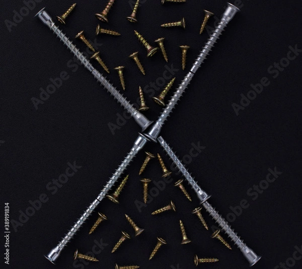 Fototapeta The abstract form and background for the text is made of self-tapping screws and furniture screws on a black background (top view).