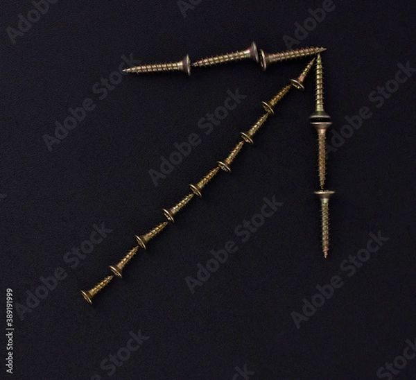 Fototapeta The outline of the pointer arrow is made of self-tapping screws on a black background (top view).