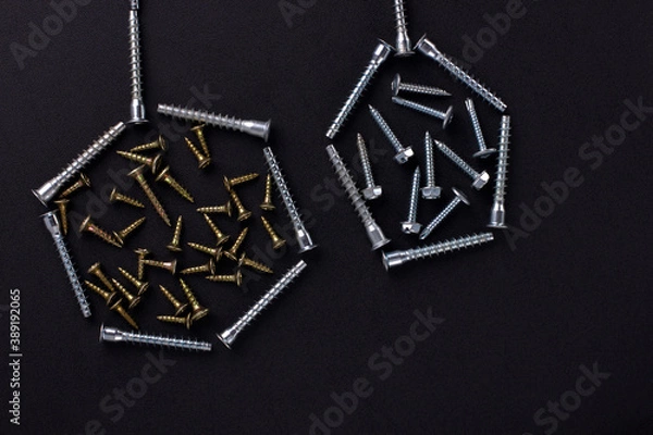 Fototapeta Abstract shapes and background for text made of self-tapping screws and furniture screws on a black background (top view).