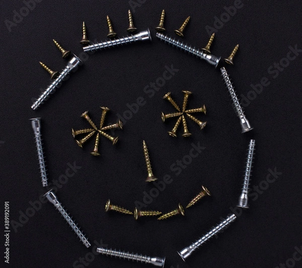 Fototapeta The outline of a smile is made of self-tapping screws on a black background (top view).