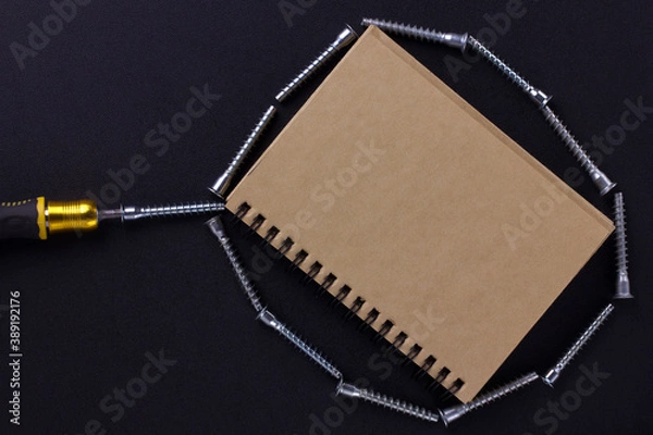 Fototapeta tools for repair and construction. Screwdriver, furniture screws, notebook on a black background with a place for text. View from above