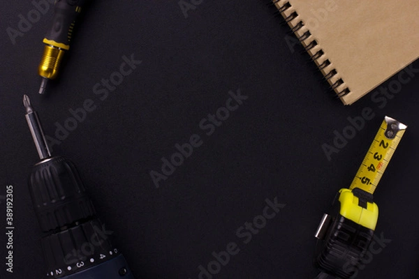 Fototapeta tools for repair and construction. Screwdriver, measuring tape, notepad on a black background with place for text. View from above