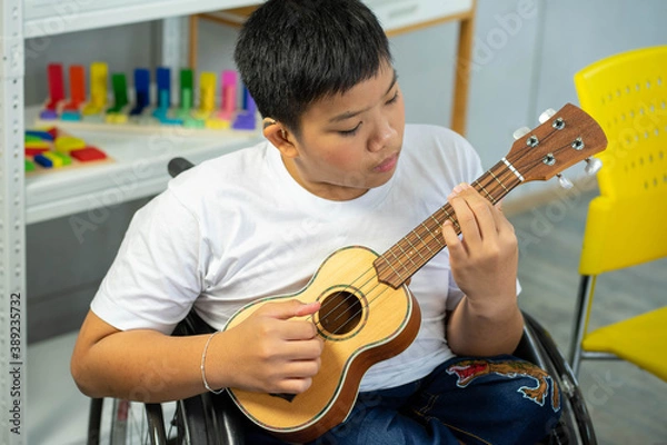 Obraz disability kid playing music with guitar on wheelchair with Autism child playing in special classroom