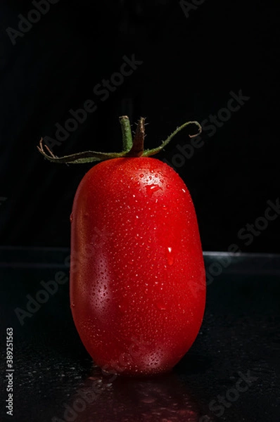 Obraz a red, fresh, ripe, juicy tomato with green leaves and drops of water on dark background with copy space for text