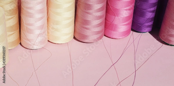 Fototapeta  Multi-colored spools of sewing thread on a pink background. Copy space for text. Horizontal format.
