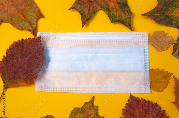 Obraz Creative composition of autumn leaves and a medical mask on a yellow background. Concept of the second wave of coronavirus infection. Postcard. Top view, space for advertising text