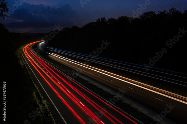 Fototapeta Long exposure white blue red and yellow light trails of cars and lorries driving on the motorway. A303 dual carriageway light trails at night