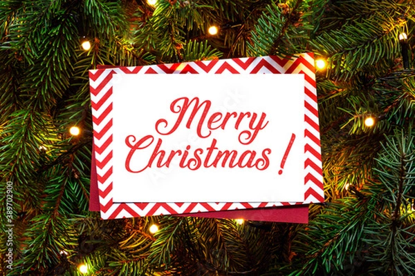 Fototapeta Christmas tree branches with paper wishing handwritten card. Nature New Year concept. Merry Christmas card, background. Congratulations, holidays, celebration. Red green and white. Ready to use, print