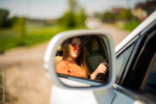 Fototapeta Close up portrait of pleasant looking female girl with, sits on driver`s seat, enjoys music. People, driving, transport concept.Portrait of beautiful young woman in the new car - outdoors