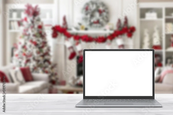 Fototapeta Blank display screen laptop computer on white wood table. Modern cozy comfortable home living room with Christmas decor. Home office desk workspace. Mock up copy space. Winter sales, online shopping