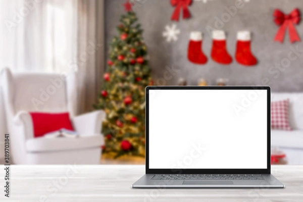 Fototapeta Blank display screen laptop computer on white wood table. Modern cozy comfortable home living room with Christmas decor. Home office desk workspace. Mock up copy space. Winter sales, online shopping