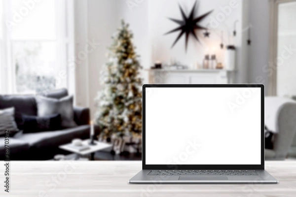 Fototapeta Blank display screen laptop computer on white wood table. Modern cozy comfortable home living room with Christmas decor. Home office desk workspace. Mock up copy space. Winter sales, online shopping