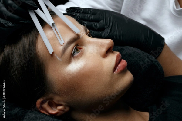 Fototapeta Beautician in gloves making measuring of eyebrows