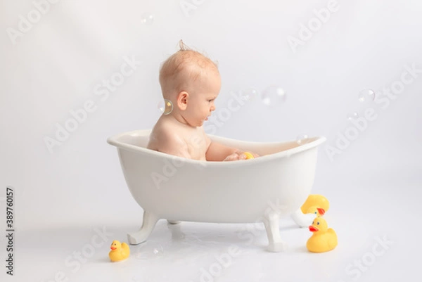 Fototapeta bathing the baby in white bath with foam and rubber ducks