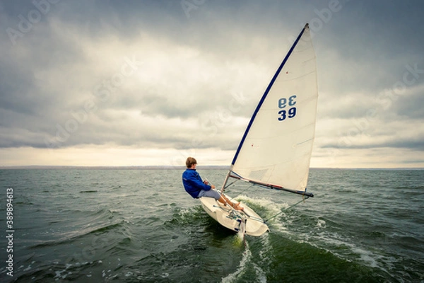 Obraz a young man on a yacht floats on the water against a cloudy sky