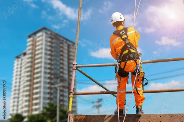 Fototapeta Safety sprinkling worker on high with scaffolding  wear dresses and safety man with harness safety concept on steel structures success from work in site construction building on blue sky background.
