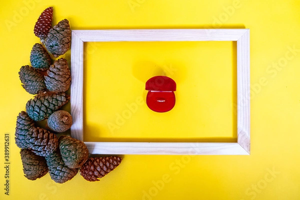 Obraz Wooden photo frame with cones and wedding ring on a yellow background