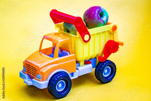 Obraz Toy truck on a yellow background with apples. Cargo transportation of fruit.